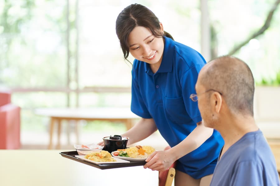 Caregiver Serving The Elderly A Meal On A Tray