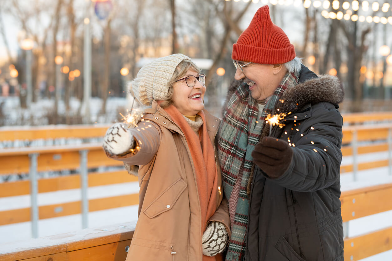 Two people wearing coats and hats enjoying sparklers on a snowy terrace as part of a winter outing